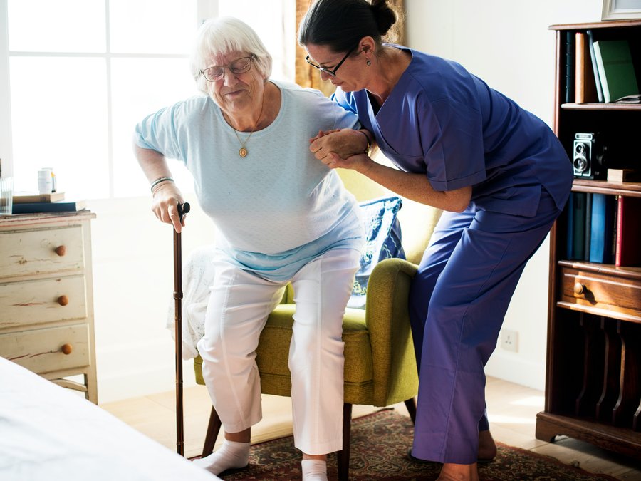 A nurse helping an older woman stand up safely at home