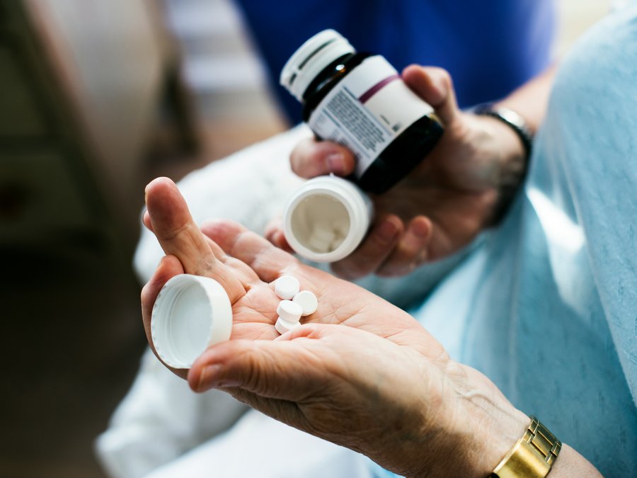 Close-up of hands holding medication tablets and a pill bottle